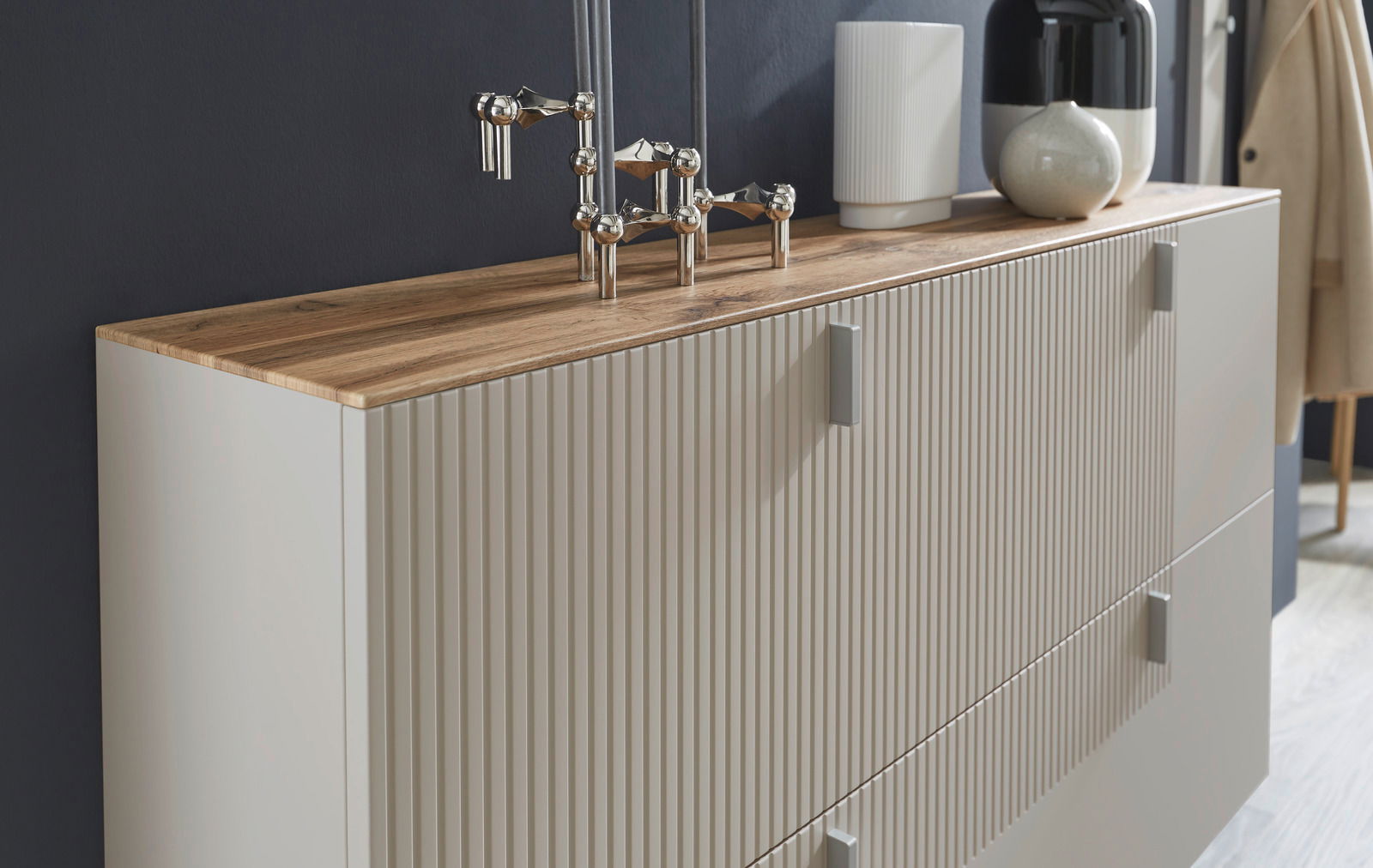 Seitliche Perspektive auf einen modernen Hängeschuhschrank mit Holzoberfläche und vertikalen Rillen an den Türen, dekoriert mit Vasen und einer Skulptur.