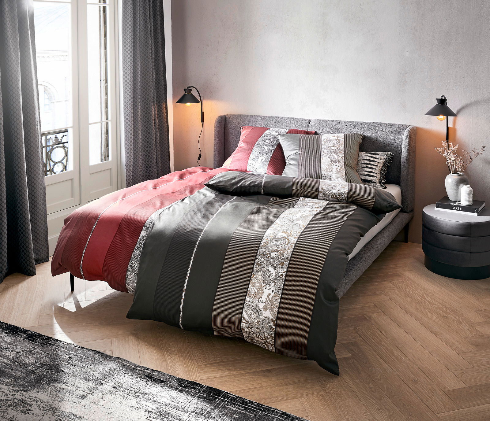 Bett mit gestreifter Bettwäsche in Rot- und Grautönen, seitliche Perspektive
