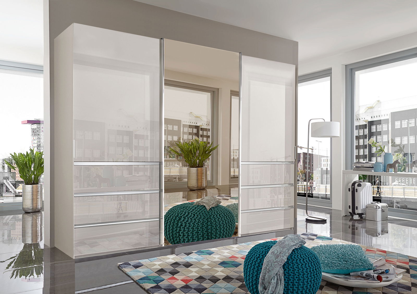Moderner Schwebetürenschrank MALIBU in einem hellen Raum mit großen Fenstern, seitliche Perspektive.