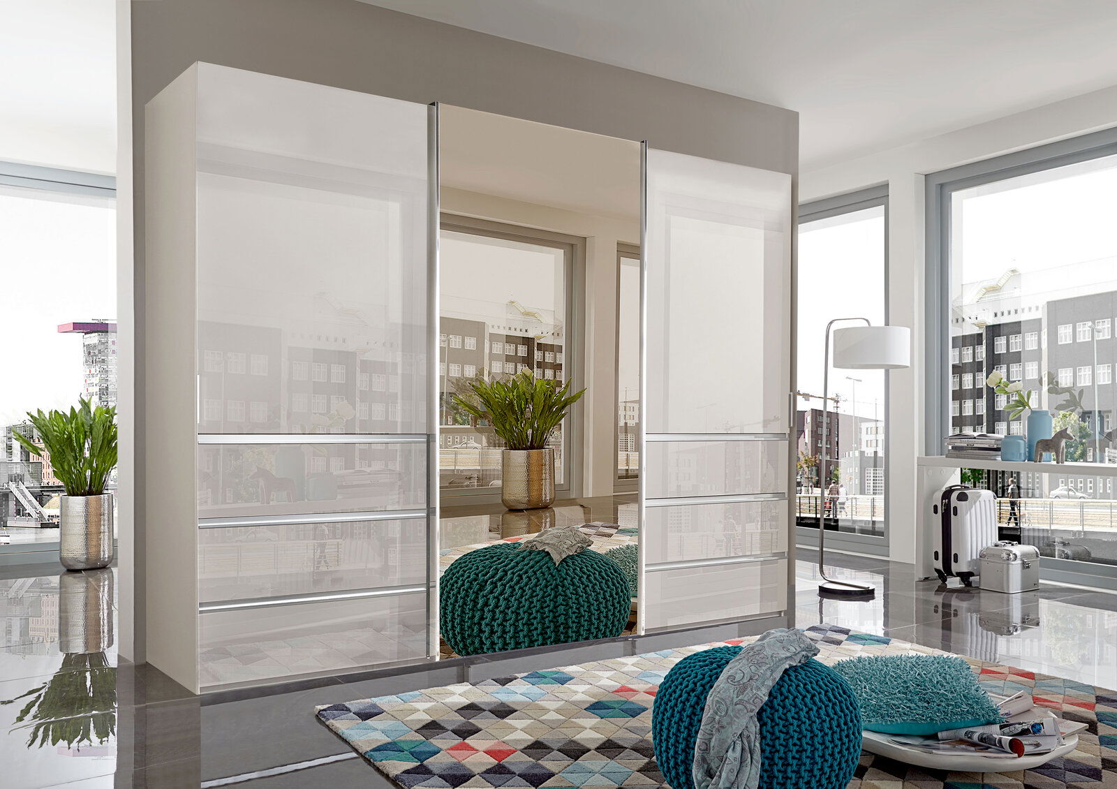 Moderner Schwebetürenschrank MALIBU in einem hellen Raum mit großen Fenstern, seitliche Perspektive.