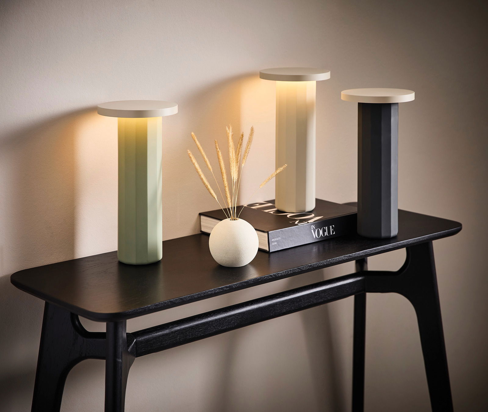 Dieter Knoll Akku-Tischleuchte Drei moderne Akku-Tischleuchten in verschiedenen Farben auf einem schwarzen Tisch, seitliche Perspektive.