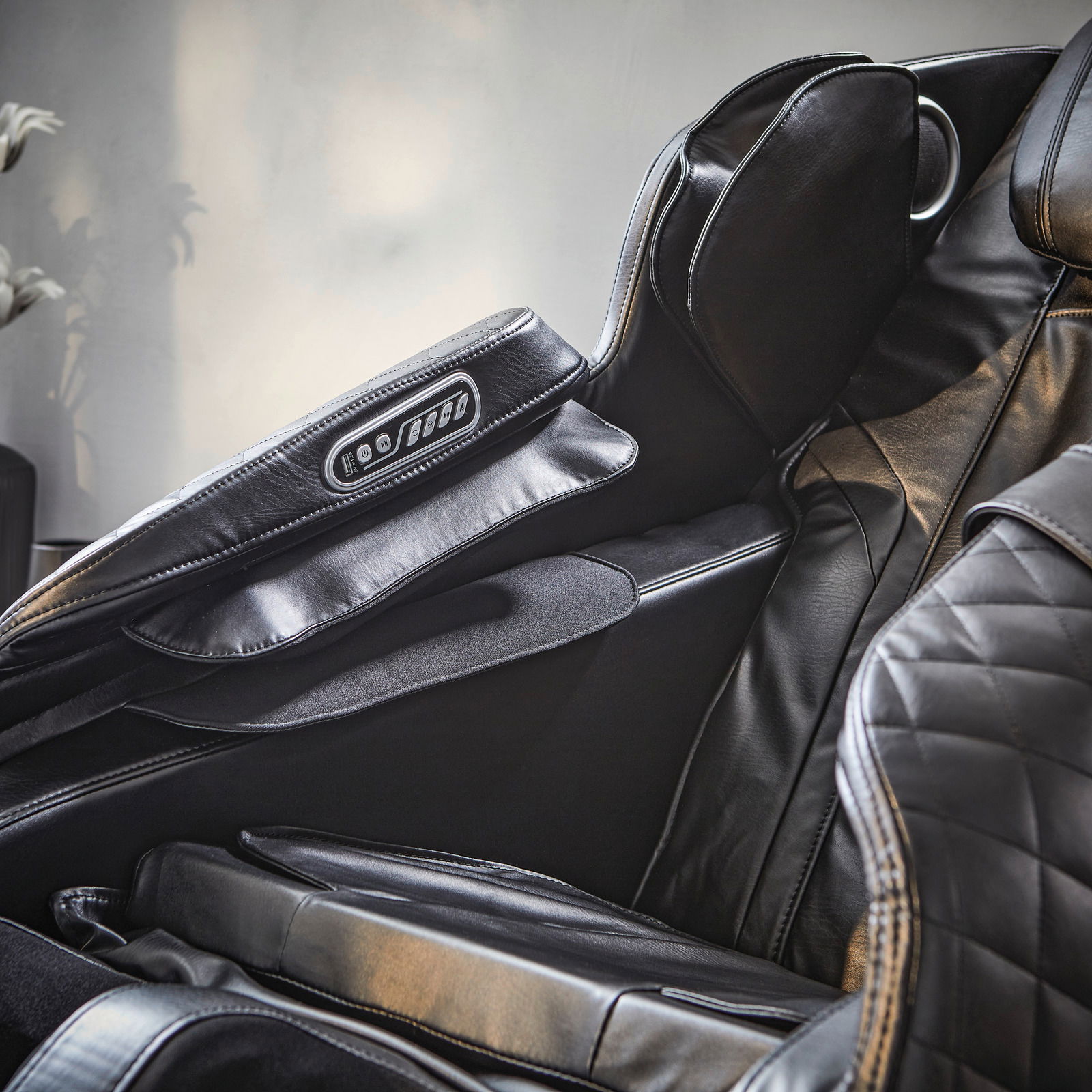 Nahaufnahme eines luxuriösen Massagesessels aus schwarzem Leder mit integrierter Steuerung an der Armlehne, seitliche Perspektive.