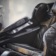 Nahaufnahme eines luxuriösen Massagesessels aus schwarzem Leder mit integrierter Steuerung an der Armlehne, seitliche Perspektive.