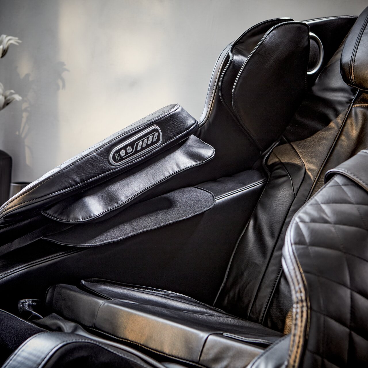 Nahaufnahme eines luxuriösen Massagesessels aus schwarzem Leder mit integrierter Steuerung an der Armlehne, seitliche Perspektive.