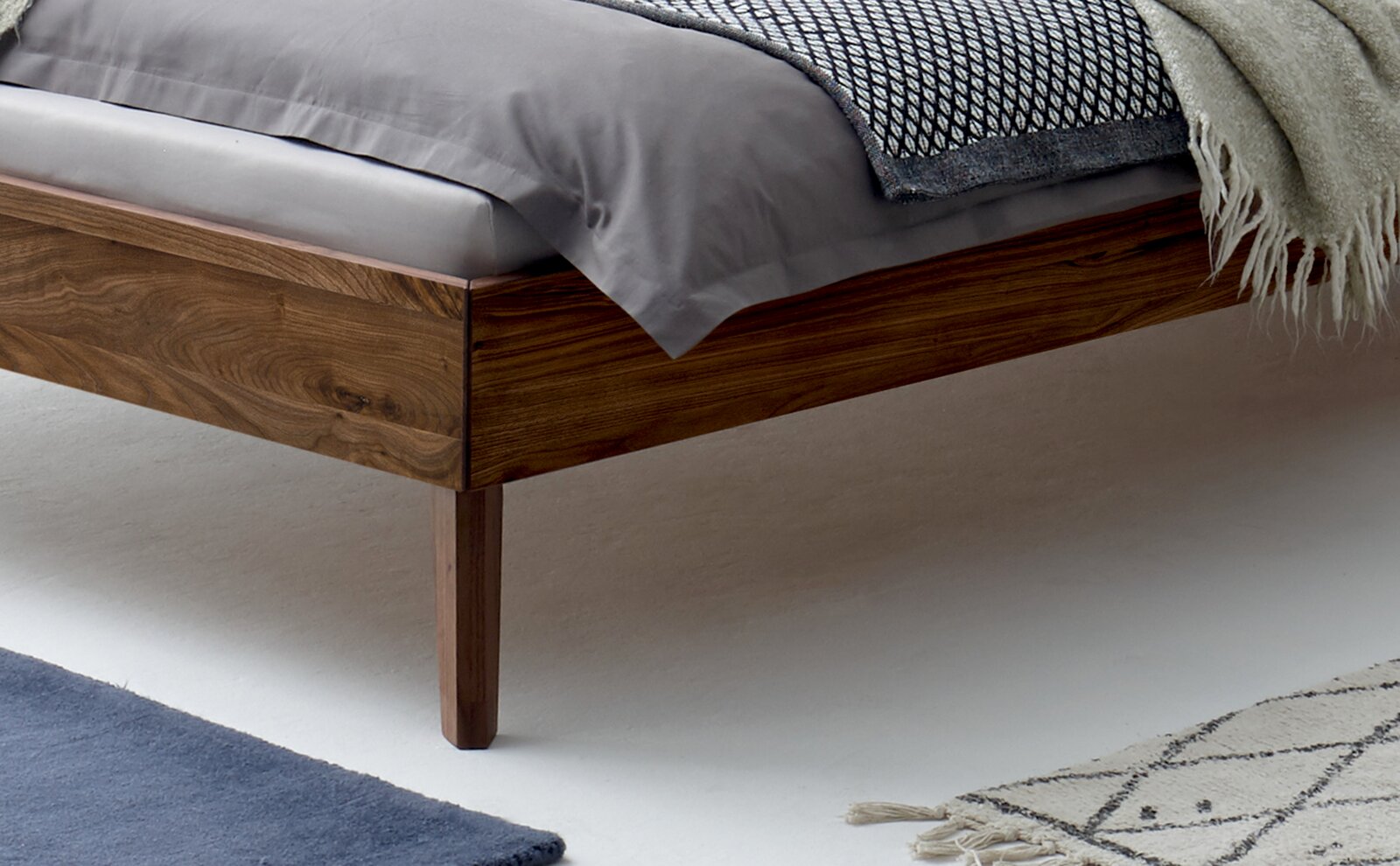 Nahaufnahme eines Bettgestells aus Holz mit Bettwäsche, seitliche Perspektive
