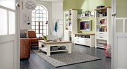 Wohnzimmer mit moderner Einrichtung, bestehend aus einem Couchtisch, einem Sideboard mit Fernseher und Regalen, in einer hellen und gemütlichen Atmosphäre. Perspektive von der Tür aus.