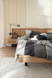 Satin-Bettwäsche in Grau- und Schwarztönen auf einem modernen Holzbett, seitliche Perspektive.