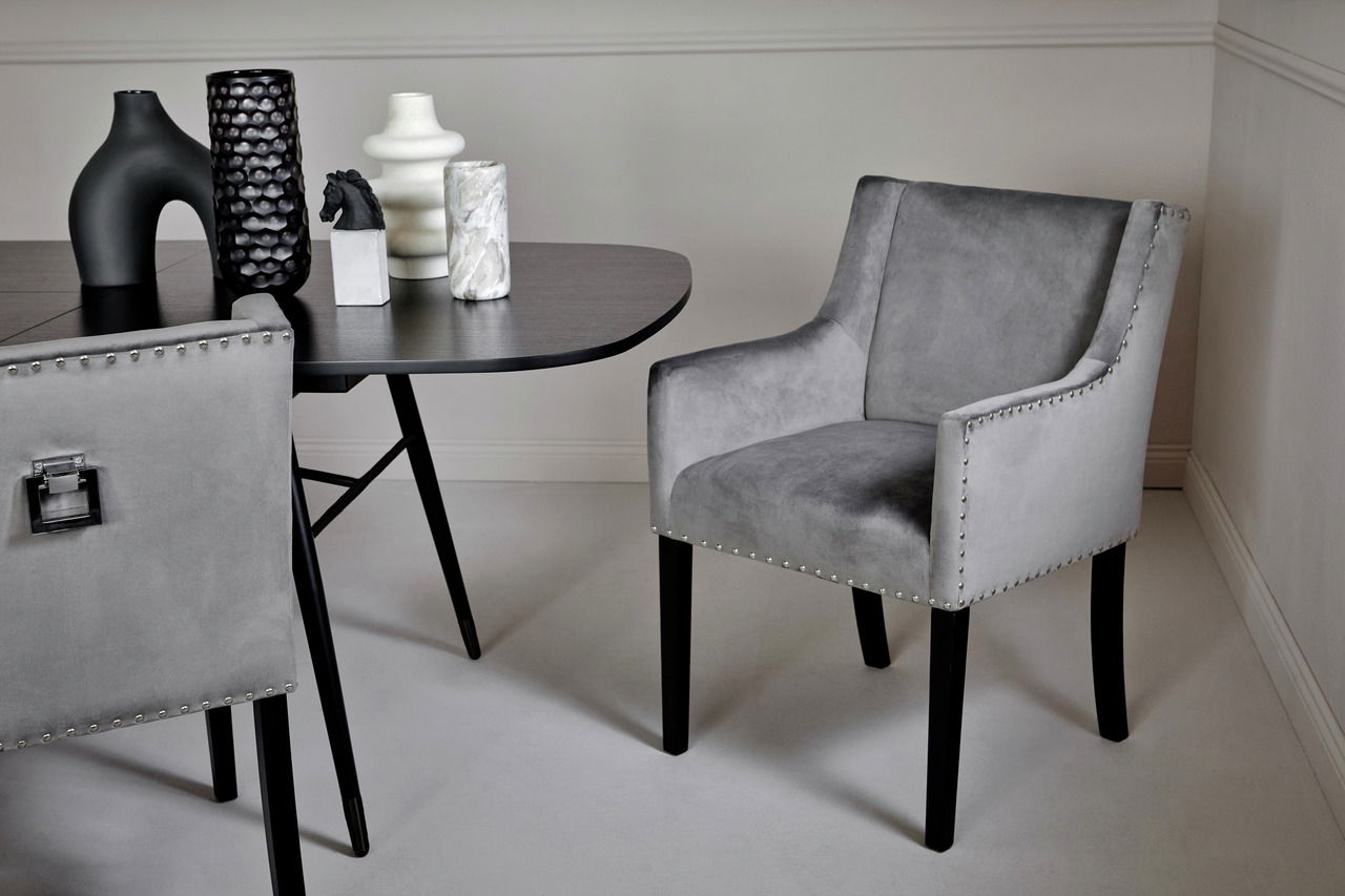 Grauer Stuhl mit Armlehnen und Nietenverzierung, seitliche Perspektive, neben einem Tisch mit dekorativen Vasen.