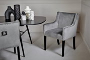 Grijze stoel met armleuningen en studs, zijaanzicht, naast een tafel met decoratieve vazen.