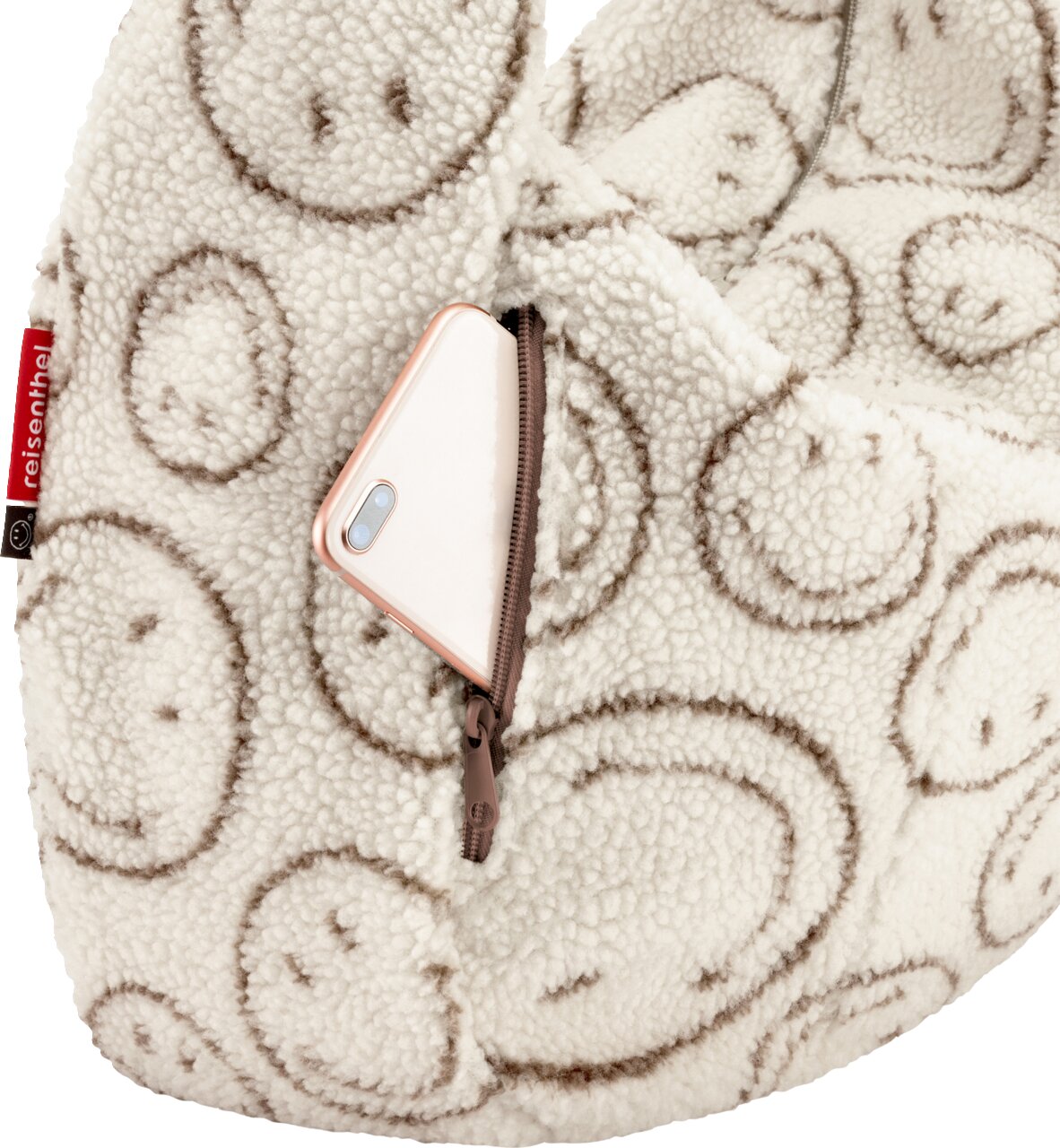 Nahaufnahme in schräger Vorderansicht: flauschiger Reißverschluss-Rucksack aus cremefarbenem Teddy-Material mit braunem Smileymuster, Fronttasche mit Reißverschluss und teilweise sichtbarem Smartphone