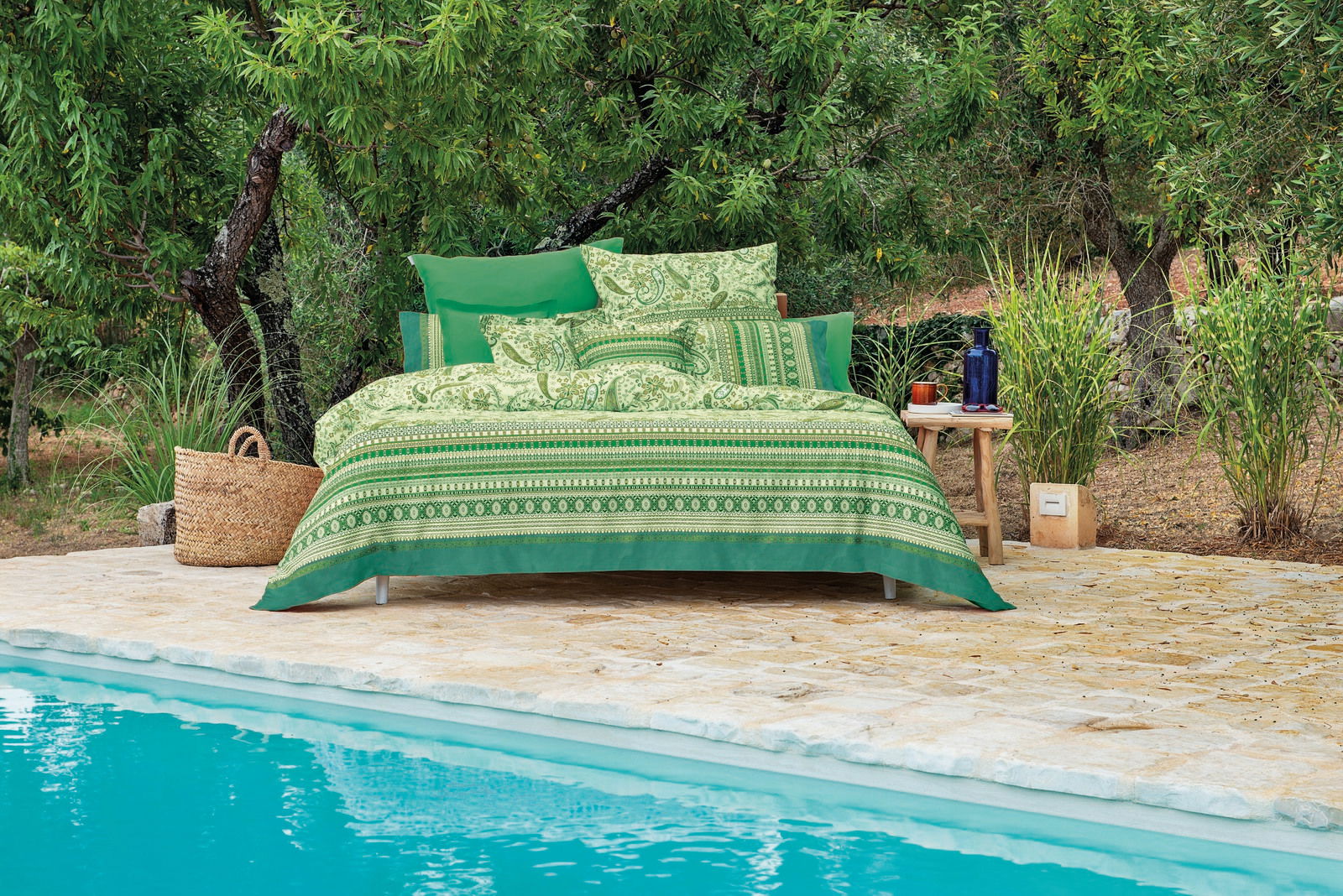 Grüne Bettwäsche 155x220cm mit dekorativem Muster, präsentiert auf einem Bett am Pool, umgeben von Bäumen und Pflanzen, aus seitlicher Perspektive.
