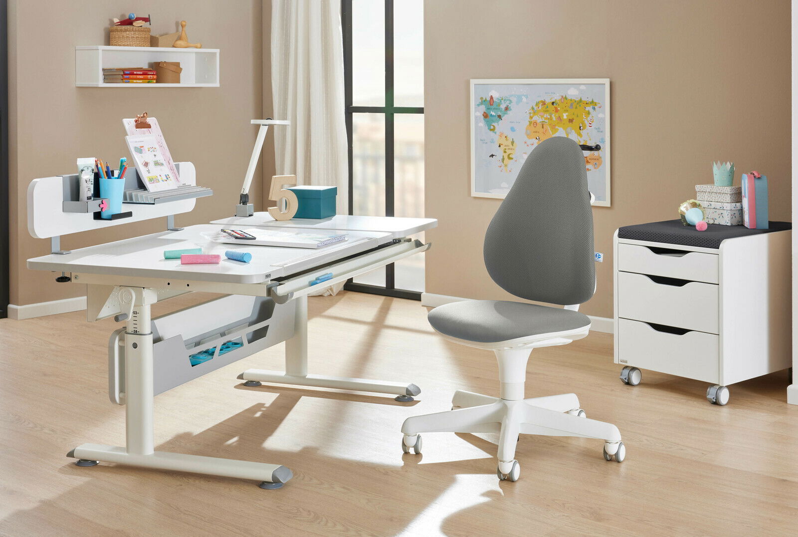 Paidi Jugenddrehstuhl JOOKI X Moderner Jugenddrehstuhl in Grau und Weiß, seitliche Perspektive, neben einem höhenverstellbaren Schreibtisch in einem hellen Raum.