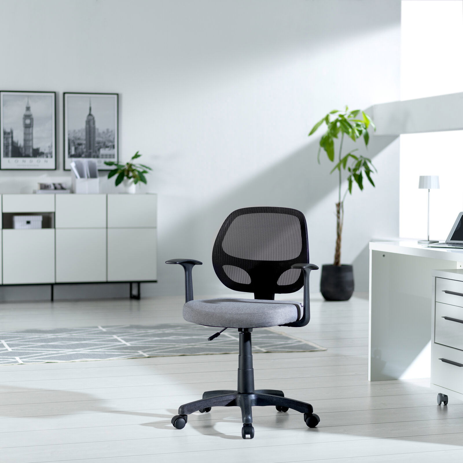 Moderner Drehstuhl mit Netzrückenlehne und grauem Sitzpolster, seitliche Perspektive in einem hellen Büro mit Pflanzen und Schreibtisch.