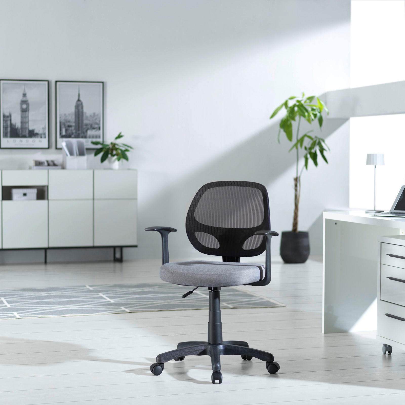 Moderner Drehstuhl mit Netzrückenlehne und grauem Sitzpolster, seitliche Perspektive in einem hellen Büro mit Pflanzen und Schreibtisch.