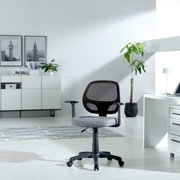 Moderne draaistoel met rugleuning van gaas en grijze zitbekleding, zijaanzicht in een licht kantoor met planten en een bureau.