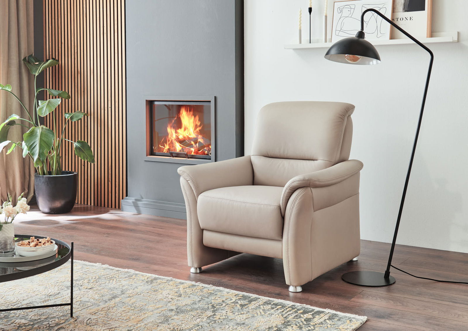 Bequemer beiger Sessel in einem modernen Wohnzimmer, seitliche Perspektive, neben einem Kamin und einer Stehlampe.