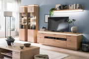 Wohnzimmer mit moderner Holzmöbelkombination, bestehend aus zwei beleuchteten Vitrinen, einem TV-Element mit Flachbildfernseher und einem Wandregal, seitliche Perspektive.