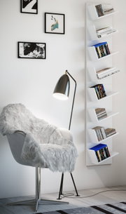 Modernes weißes Wandregal mit mehreren schrägen Ablagefächern, bestückt mit Büchern und DVDs, seitliche Frontansicht im Wohnraum neben Sessel und Stehlampe