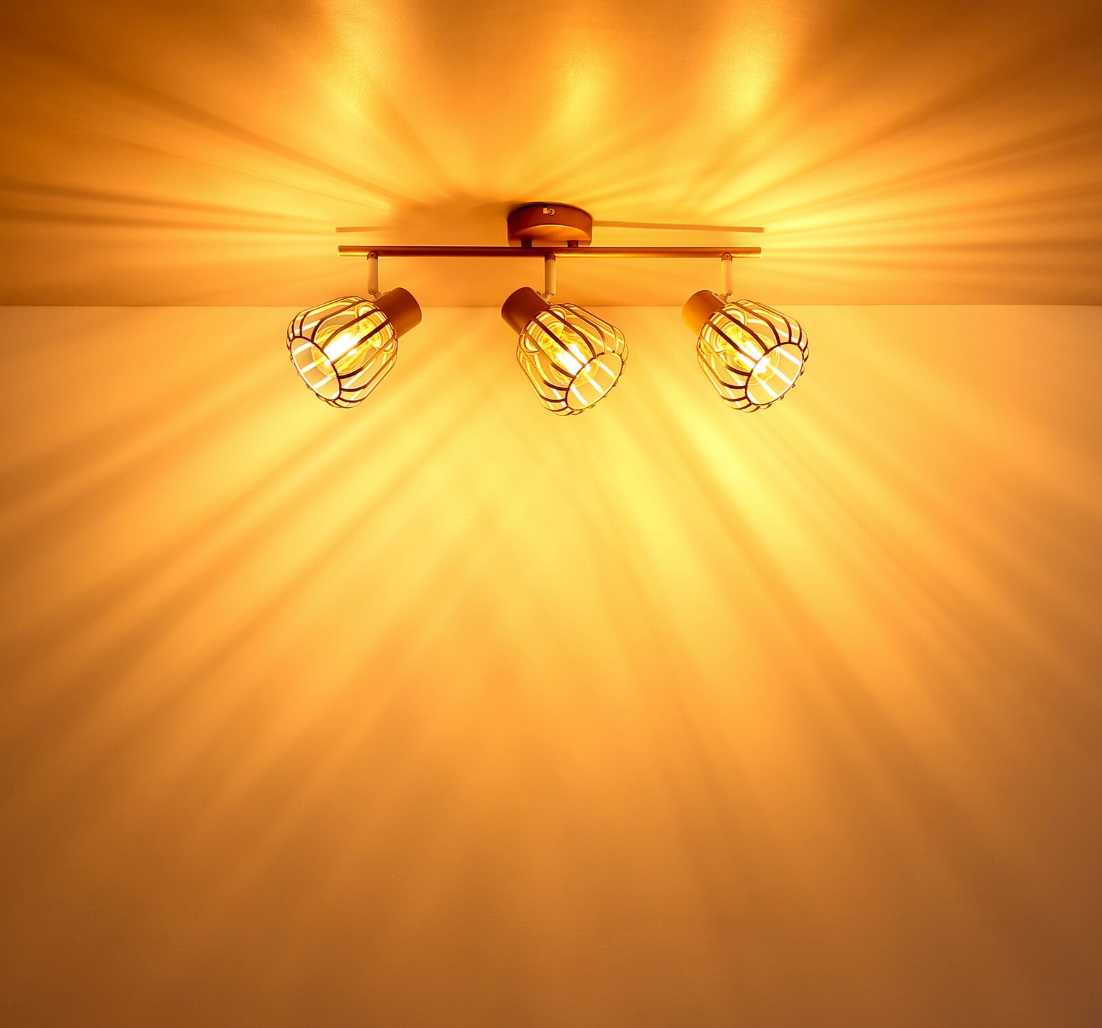 Dreiflammige Deckenleuchte mit Metallkäfig-Schirmen und warm leuchtenden Edison-Glühbirnen, frontal von unten an der Decke fotografiert, mit strahlenförmigem Lichtmuster an der Decke.