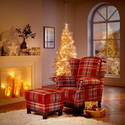 Vooraanzicht van een comfortabele rode fauteuil met klassiek ruitpatroon en bijpassende hocker in een sfeervol verlichte kerstsetting.