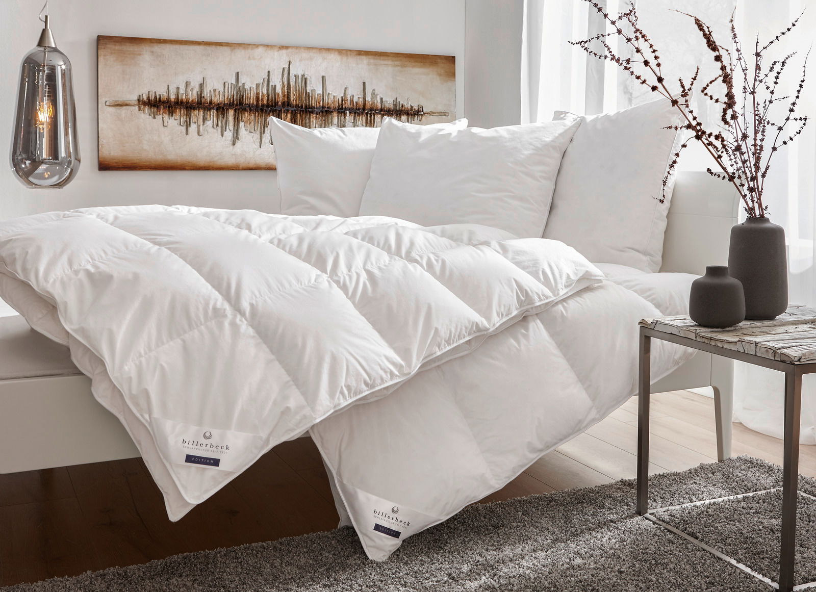 Gemütliches Schlafzimmer mit einer weißen Daunendecke und Kissen auf einem Bett, seitliche Perspektive.