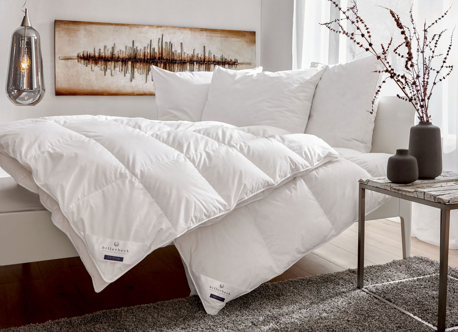 Gemütliches Schlafzimmer mit einer weißen Daunendecke und Kissen auf einem Bett, seitliche Perspektive.