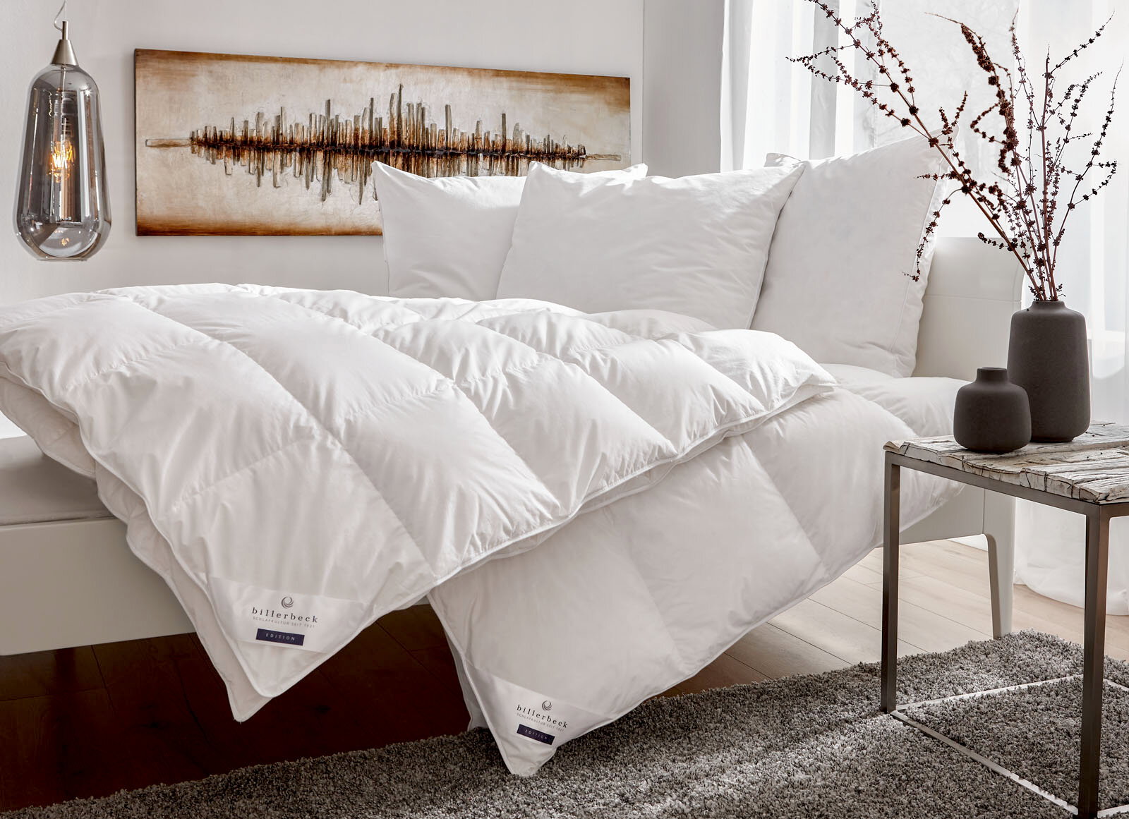 Gemütliches Schlafzimmer mit einer weißen Daunendecke und Kissen auf einem Bett, seitliche Perspektive.