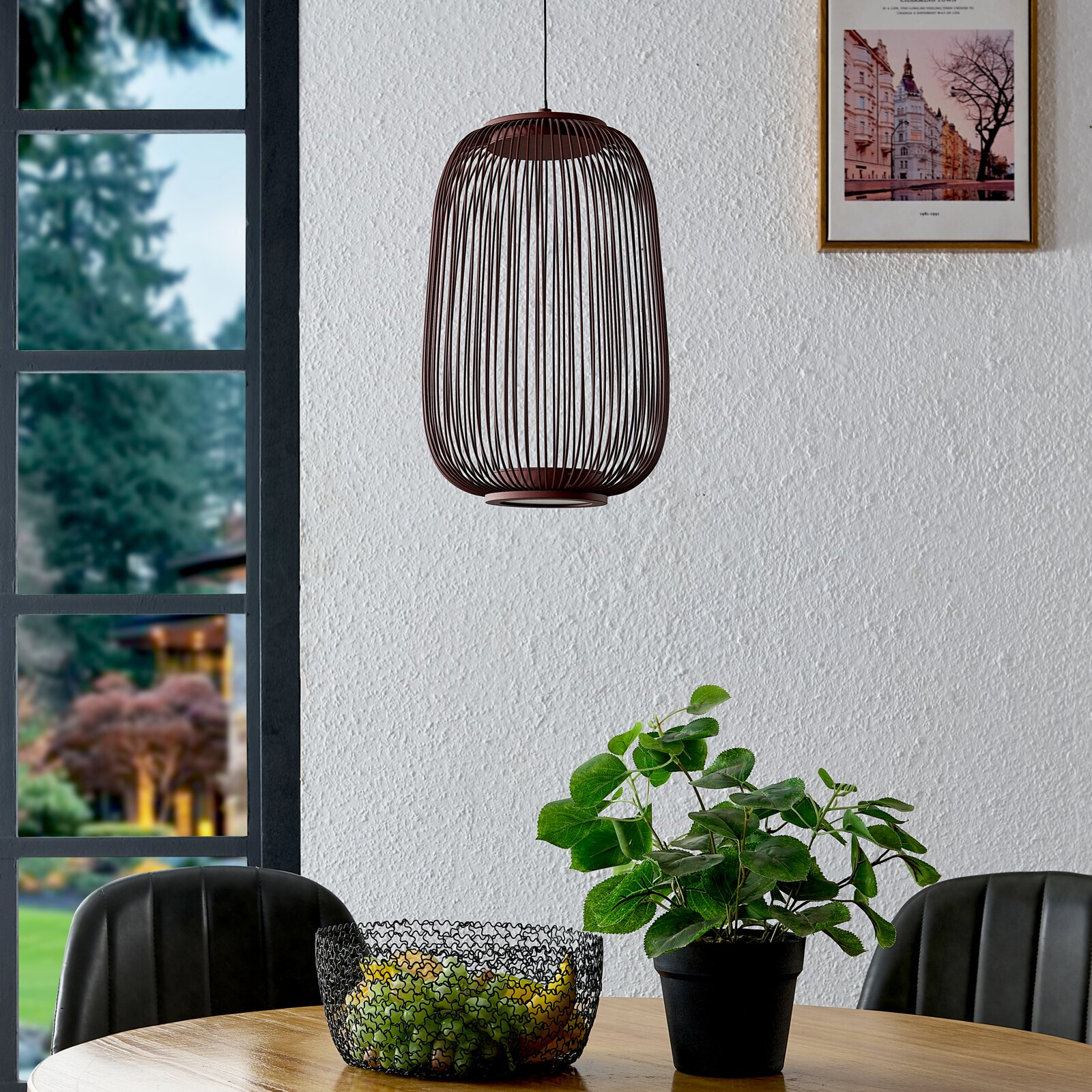 Braune, ovale Pendelleuchte mit offenem Draht-Lampenschirm hängt vor einer hellen Wand über einem Esstisch; Perspektive: frontale Ansicht auf Augenhöhe.