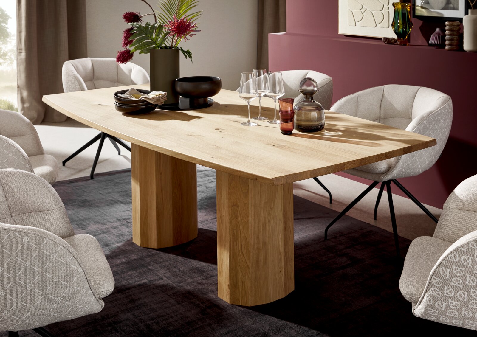Rechteckiger Esstisch aus hellem Massivholz mit dicker Tischplatte und zwei blockförmigen Säulenfüßen, dekoriert mit Gläsern und Vase, in schräger Frontansicht im modern eingerichteten Esszimmer.