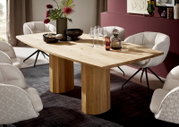 Rechteckiger Esstisch aus hellem Massivholz mit dicker Tischplatte und zwei blockförmigen Säulenfüßen, dekoriert mit Gläsern und Vase, in schräger Frontansicht im modern eingerichteten Esszimmer.