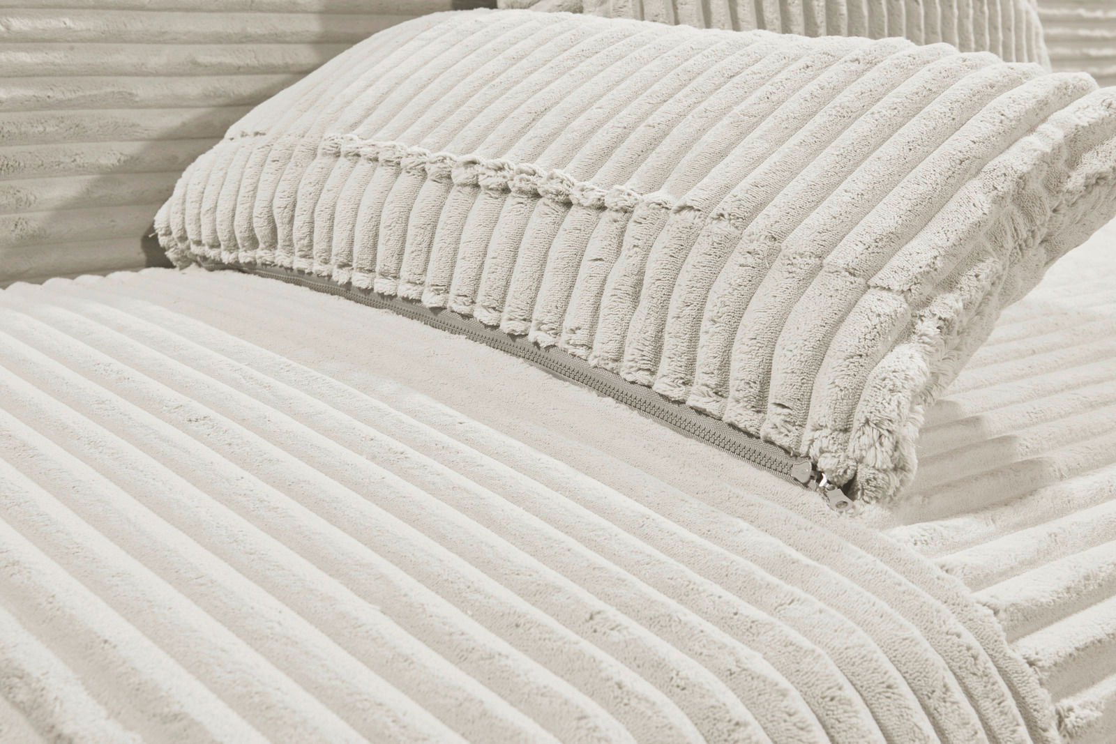 Nahaufnahme eines Funktionssofas mit weichem, geripptem Stoffbezug in hellem Beige, Perspektive von der Seite.