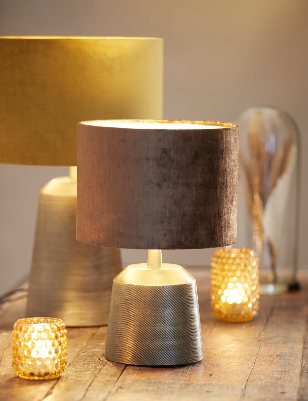 Light&Living Lampenfuß LILOU Zwei stilvolle Tischlampen mit metallischen Lampenfüßen und samtigen Lampenschirmen in warmen Farben, umgeben von dekorativen Teelichtern auf einem Holztisch, seitliche Perspektive.