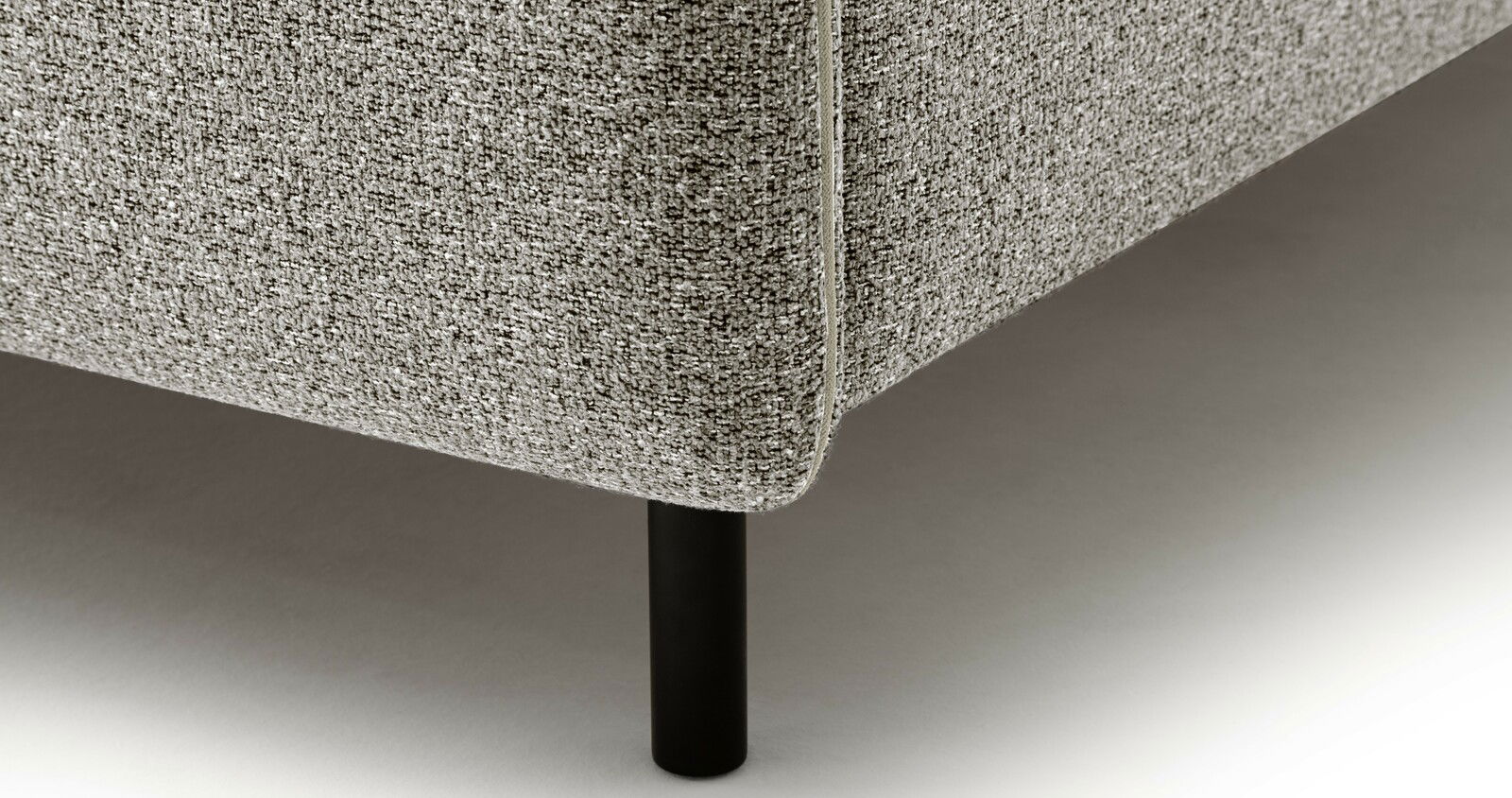 Nahaufnahme eines Polsterbetts mit grauem Stoffbezug und schwarzem Bein, seitliche Perspektive