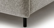Close-up van een gestoffeerd bed met grijze bekleding en zwarte poten, gezien vanaf de zijkant
