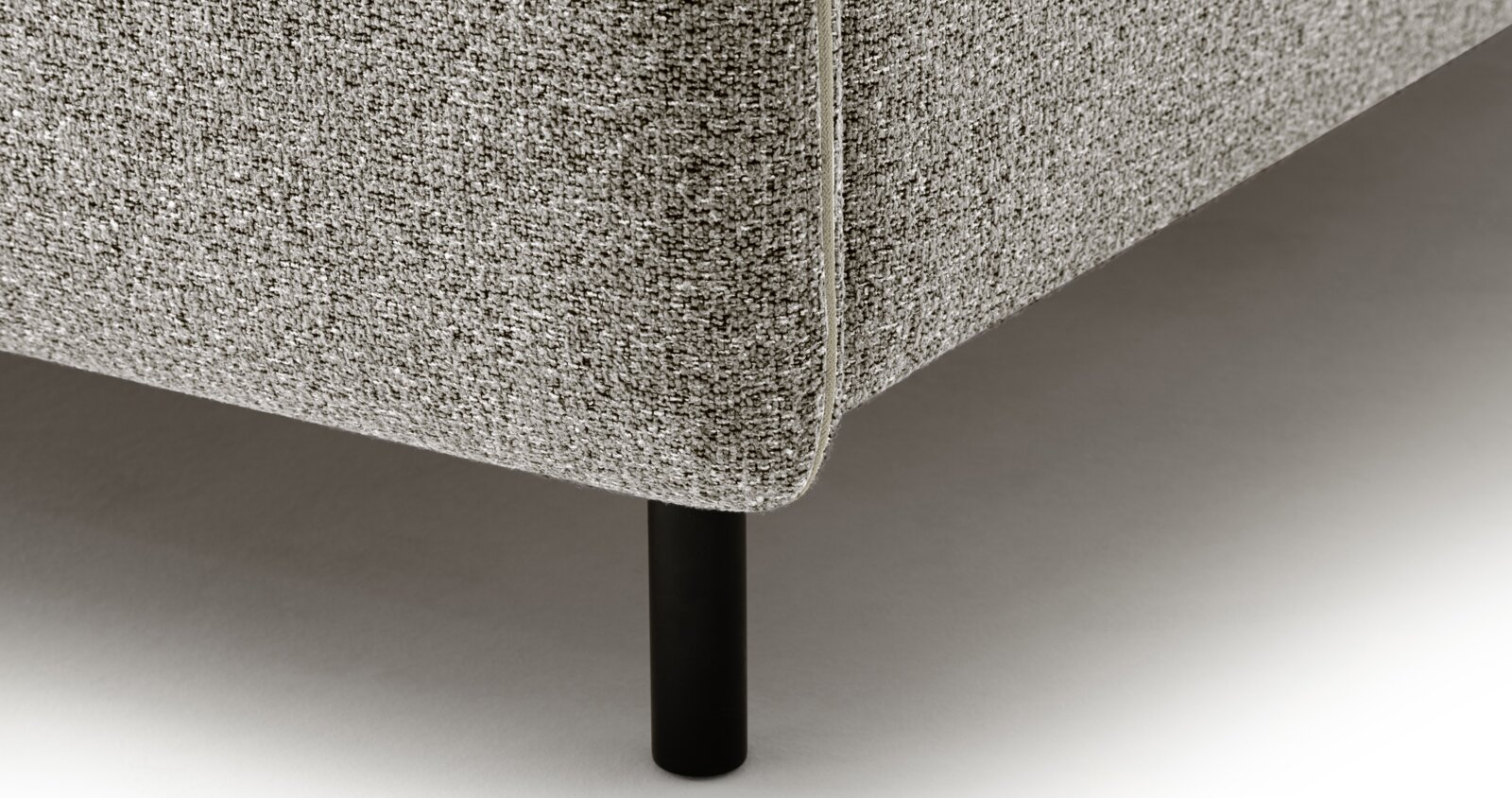 Close-up van een gestoffeerd bed met grijze bekleding en zwarte poten, gezien vanaf de zijkant