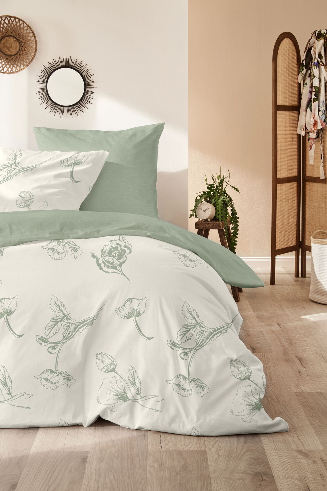 Bettwäsche-Set in sanftem Grün mit floralem Muster, auf einem Bett in einem hellen Raum mit Pflanzen und Dekorationen, aus der Vorderansicht fotografiert.