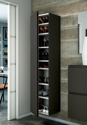 Moderner Hänge-Garderobenschrank in dunklem Design, gefüllt mit Schuhen, an einer Betonwand montiert. Perspektive von vorne links.