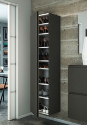 Moderner Hänge-Garderobenschrank in dunklem Design, gefüllt mit Schuhen, an einer Betonwand montiert. Perspektive von vorne links.