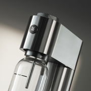 Nahaufnahme eines eleganten Wassersprudlers aus Edelstahl mit einer Glasflasche, seitliche Perspektive.