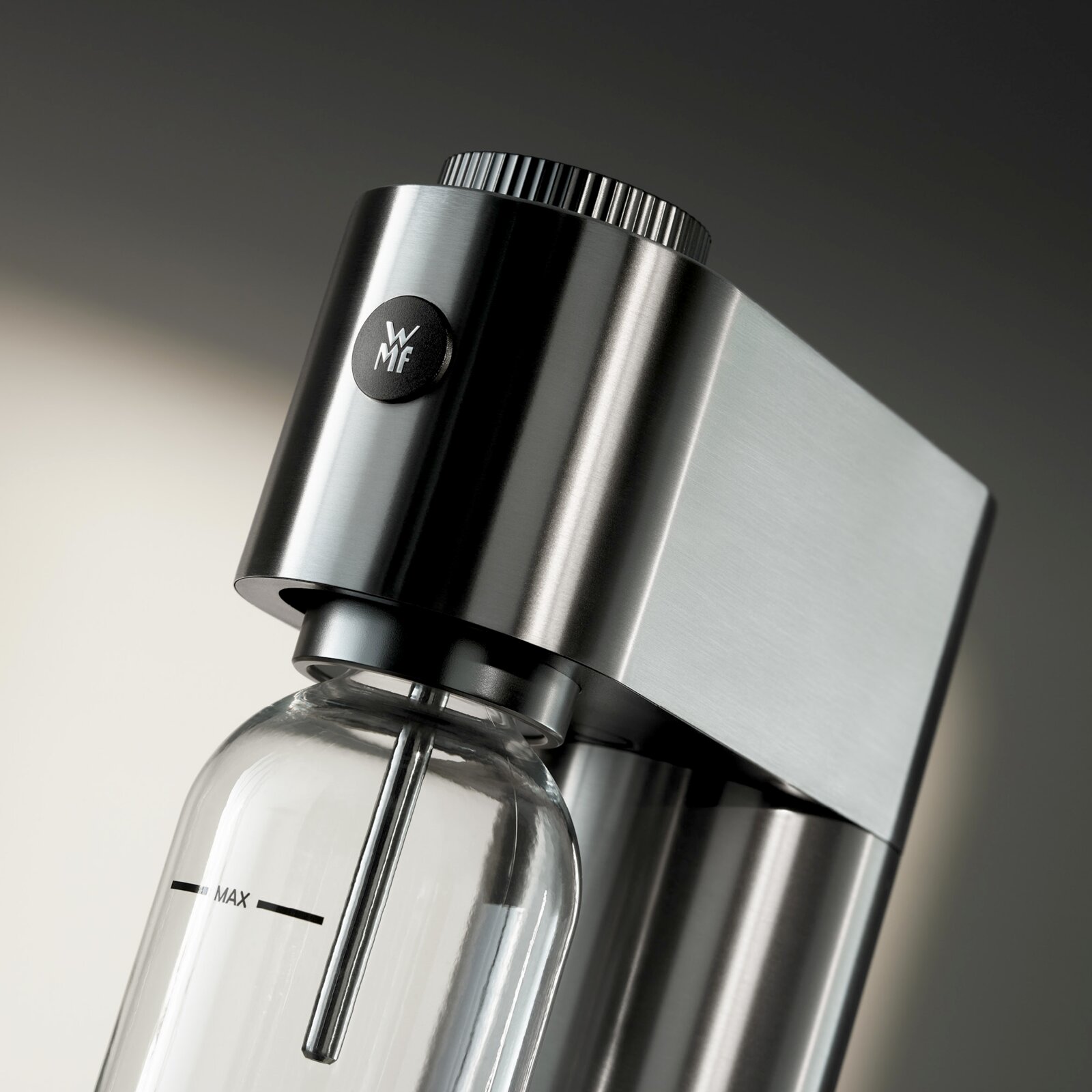 WMF Bruiswatermaker STEEL ELEMENT ONE Close-up van een elegante roestvrijstalen koolzuurapparaat met een glazen fles, gezien vanaf de zijkant.