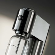 Close-up van een elegante roestvrijstalen koolzuurapparaat met een glazen fles, gezien vanaf de zijkant.