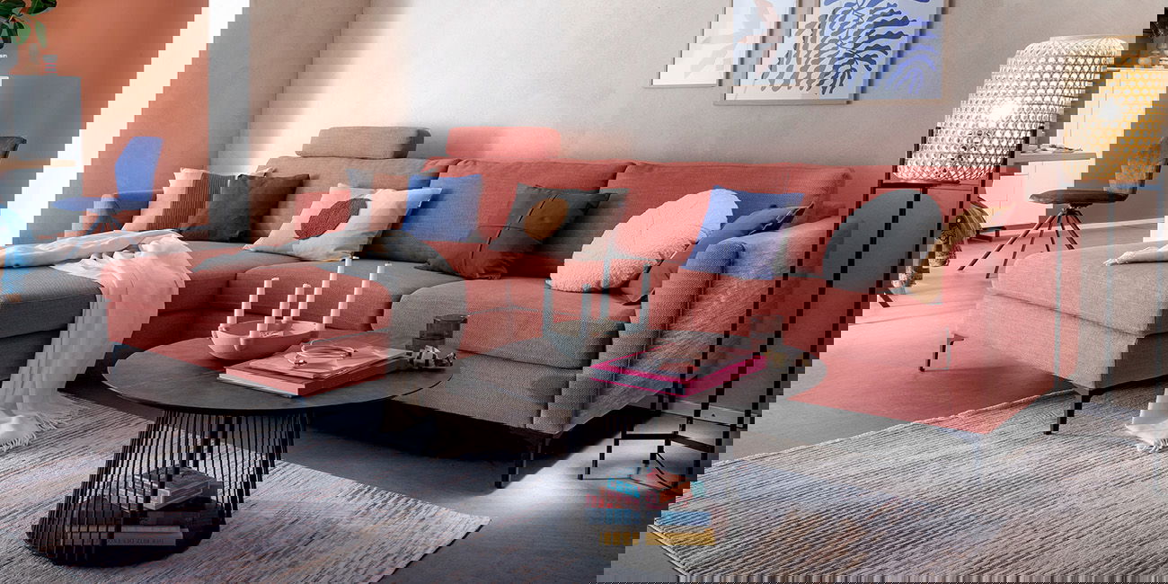 Ein Wohnzimmer mit einem korallenfarbenen Sofa, bunten Kissen und einem runden schwarzen Couchtisch.