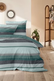Bettwäsche-Set in Blau- und Grautönen mit Streifenmuster, auf einem Bett in einem gemütlichen Schlafzimmer mit Holzboden und Dekorationen, aus der Seitenperspektive fotografiert.