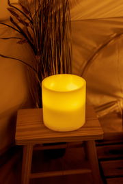 Leuchtende Outdoor-Kerze auf einem Holzhocker, umgeben von Pflanzen, aus seitlicher Perspektive fotografiert.