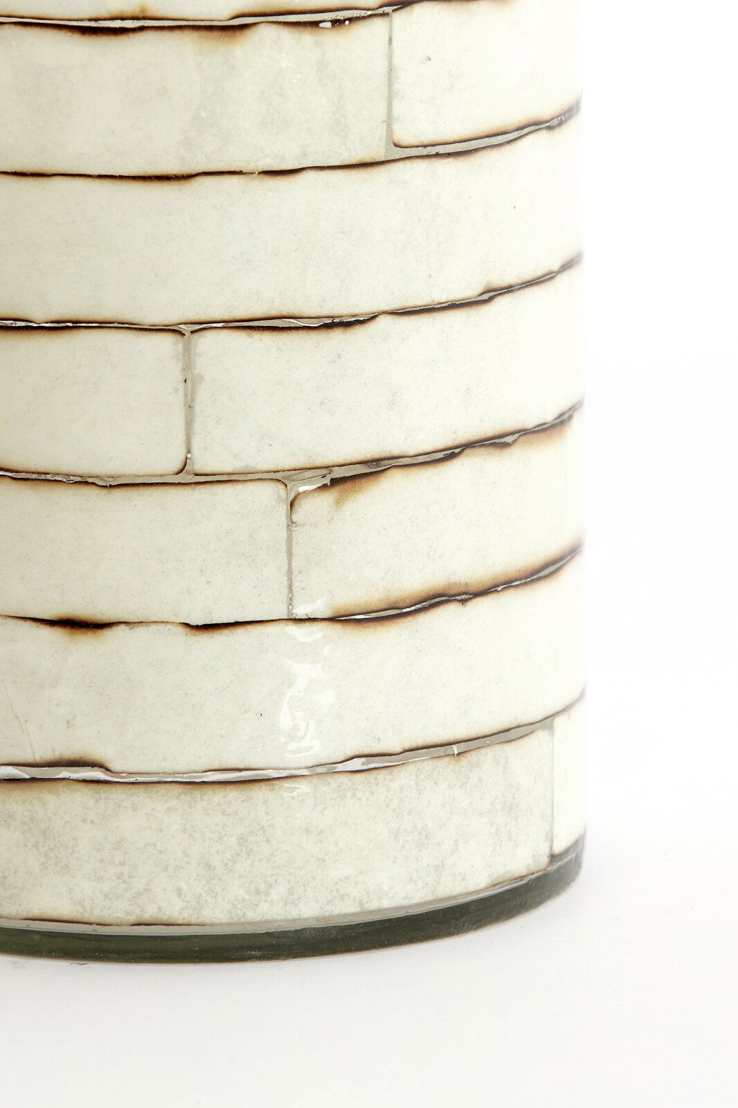 Nahaufnahme eines Teelichthalters mit cremefarbenen, rechteckigen Keramikfliesen und dunklen Fugen, seitliche Perspektive.