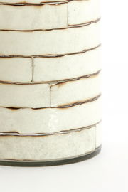 Nahaufnahme eines Teelichthalters mit cremefarbenen, rechteckigen Keramikfliesen und dunklen Fugen, seitliche Perspektive.