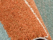 Nahaufnahme eines orangefarbenen Frisé-Teppichs mit einer weißen Linie, teilweise aufgerollt auf einem grünlichen Hintergrund.