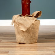 Nahaufnahme eines in Jute eingewickelten Baumstamms auf einem Holzboden, perspektivisch von vorne betrachtet.