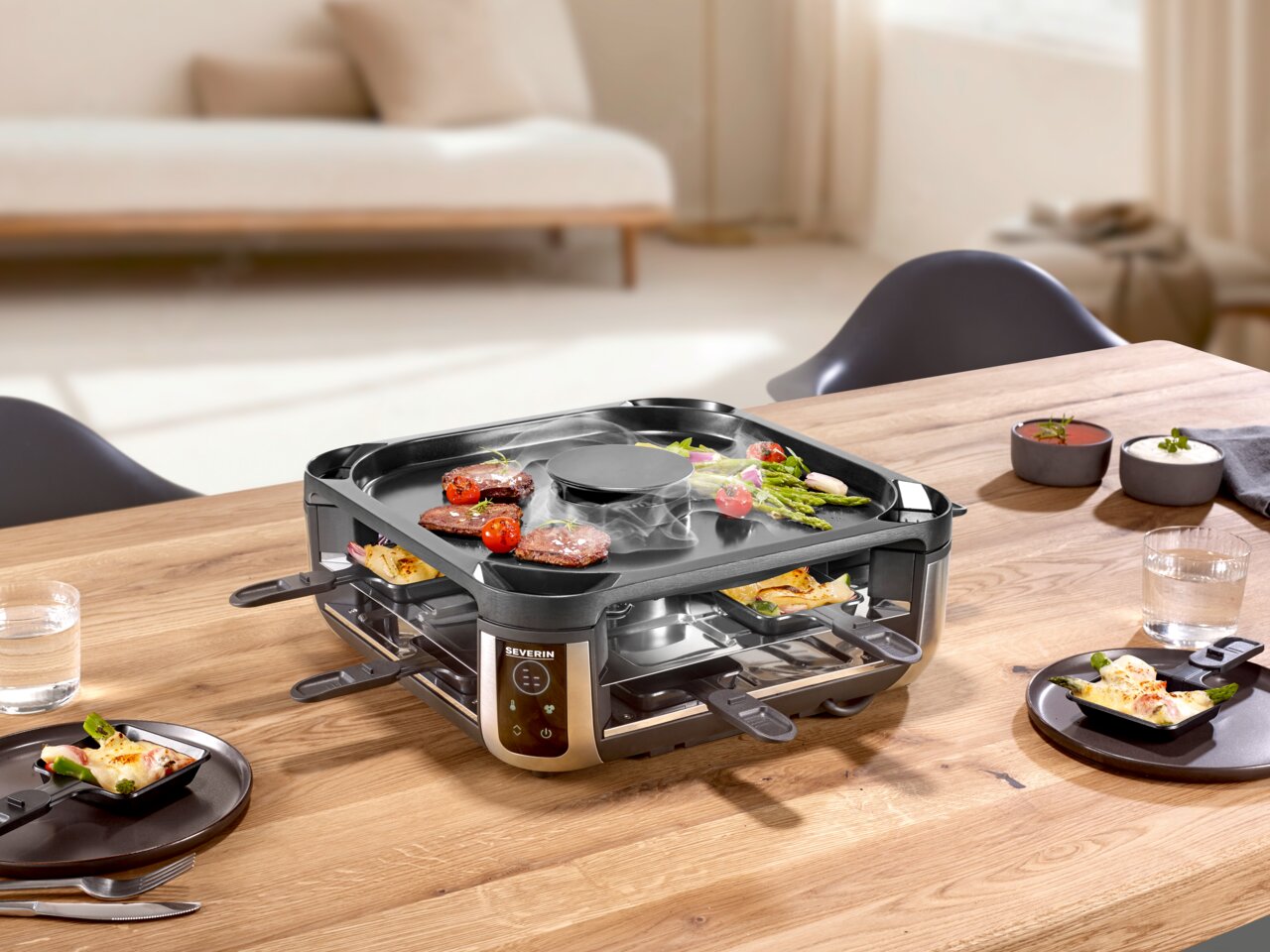 Severin Smokeless Raclette Smokeless Raclette-Grill auf einem Tisch, von schräg oben fotografiert, mit Grillgut und Pfännchen.