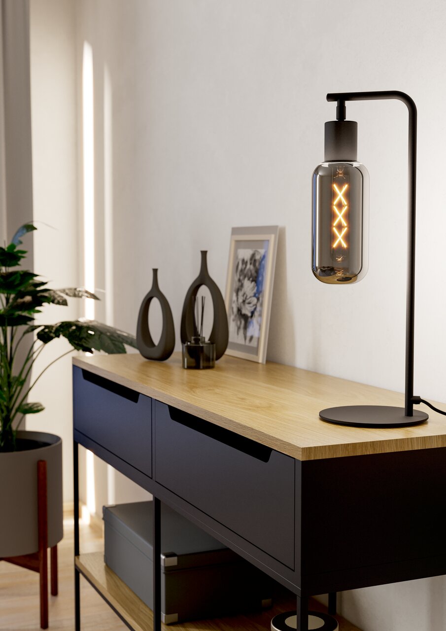 Moderne Tischleuchte MAIONE mit schwarzem Gestell und dekorativer Glühbirne, seitliche Perspektive auf einem Holztisch.